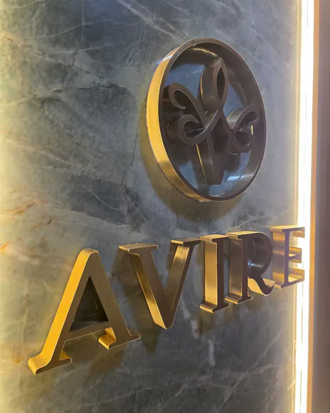 Letreiro da Avire em letras douradas sobre parede de mármore iluminada